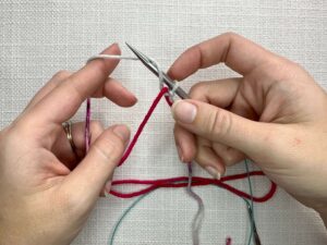 Provisional Cast On Without Crochet Hook: Move the working yarn over the needle and down the back, finally bringing it over the front of the scrap yarn again.