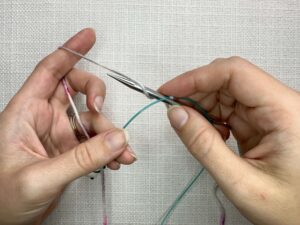 Provisional Cast On Without Crochet Hook: Scoop the yarn forward under the cord and pull the needle back up above the cord.