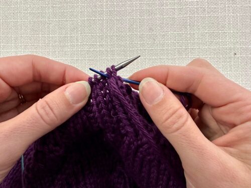 Skipping the knit stitch on your knitting needle, go behind your work, and insert your tapestry needle into the first purl stitch purlwise from the back of the work to the front.
