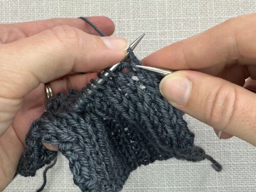 Kb1 in Knitting Step 1. Insert the right-hand needle beneath the horizontal bar and between the two legs of the stitch below the left-hand needle from front to the back.
