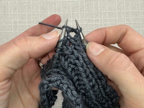 Kb1 in Knitting Step 3. Pull the yarn back through both legs of the stitch, taking care to come back beneath the horizontal bar of the stitch below the needle and not through the working stitch.