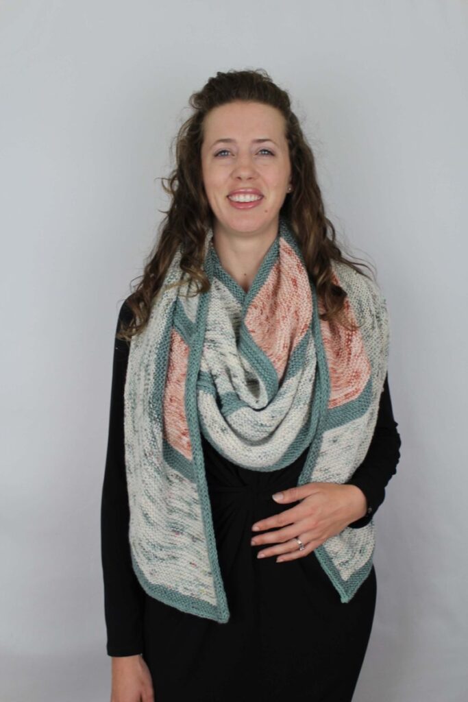 Megan wearing One Cloudy Night, an easy garter stitch shawl knitting pattern in peach, pale speckled yarn, and teal.